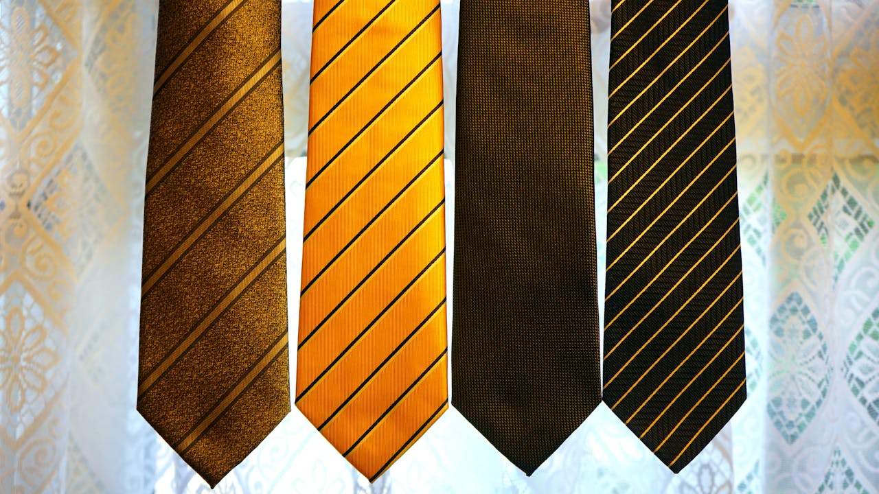 Four elegant striped ties hanging against a patterned background, showcasing modern men’s fashion.